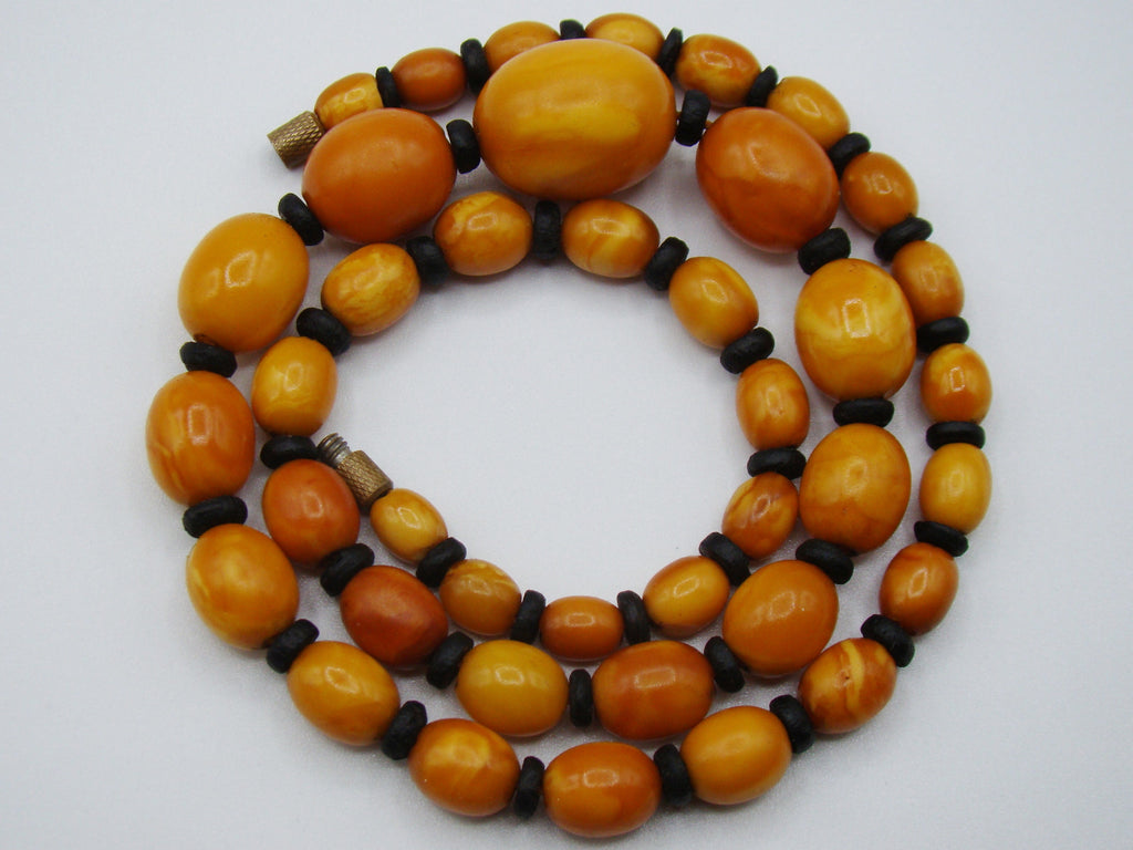 baltic amber, amber, antique, amber beads, egg Yolk, amber chain, Rosary beads, مسبحة, Masbaha, Muslim prayer beads حبيت الدورة ,العنبر الهندى, A multi-strand beaded necklace featuring polished oval amber-orange beads separated by small dark brown spacer beads, with two small metallic spacers, displayed on a light gray background.