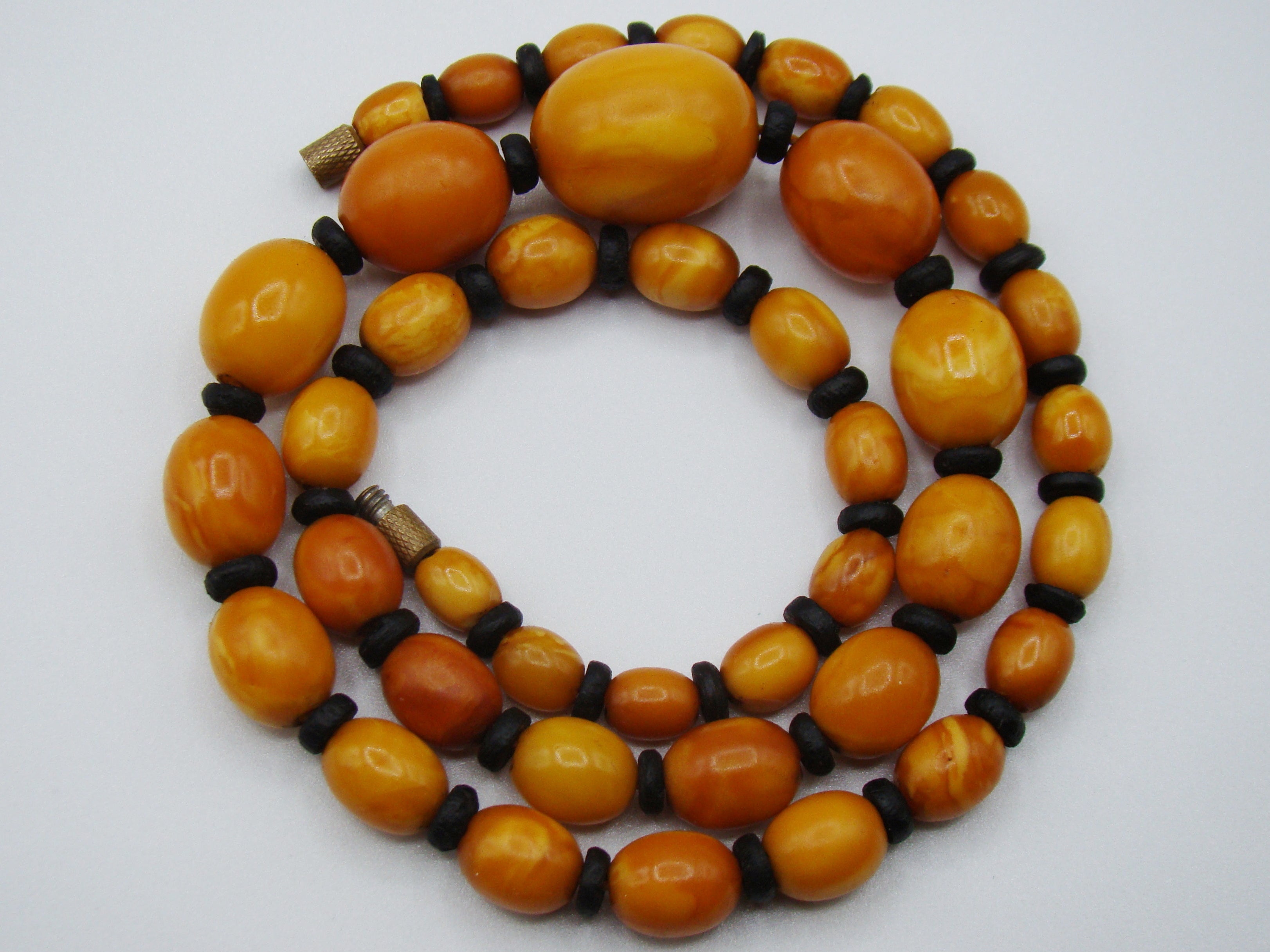 baltic amber, amber, antique, amber beads, egg Yolk, amber chain, Rosary beads, مسبحة, Masbaha, Muslim prayer beads حبيت الدورة ,العنبر الهندى, A multi-strand beaded necklace featuring polished oval amber-orange beads separated by small dark brown spacer beads, with two small metallic spacers, displayed on a light gray background.