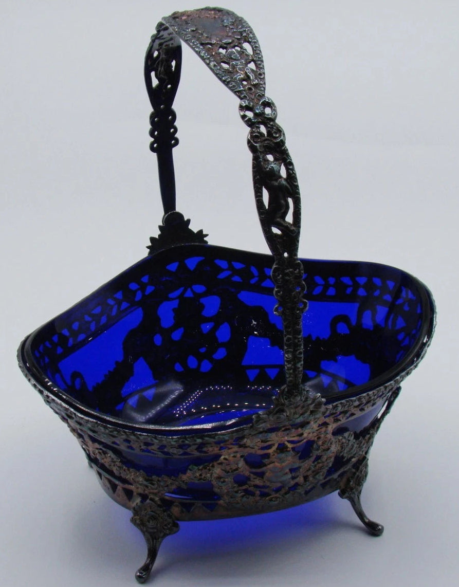 800 silver basket with cobalt-blue glass liner, ornate arched handle and curved feet, viewed at an angle.