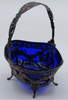 Three-quarter view of the silver basket showing its deep blue glass liner and decorated handle.