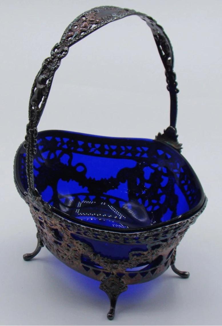 Three-quarter view of the silver basket showing its deep blue glass liner and decorated handle.