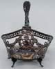Silver basket frame without its glass liner, showing pierced floral scrollwork, figural decoration and curved feet.