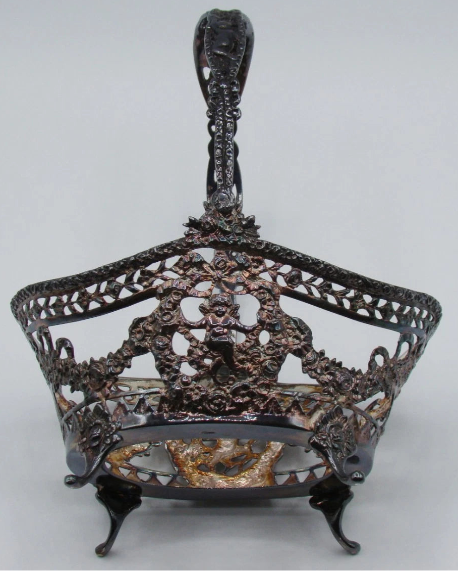 Silver basket frame without its glass liner, showing pierced floral scrollwork, figural decoration and curved feet.