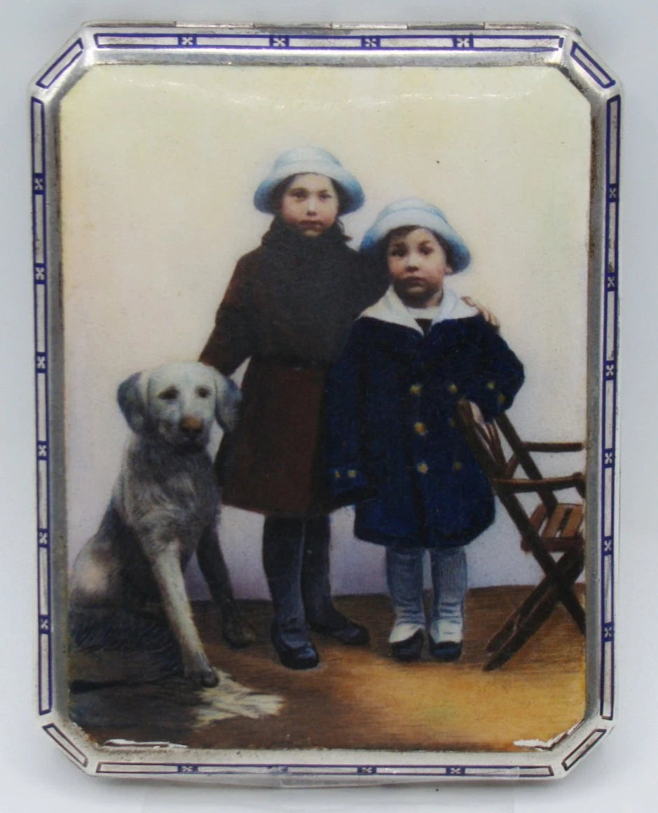 900 silver cigarette case with a colourful scene of two children and a dog, framed by a blue-and-white border.