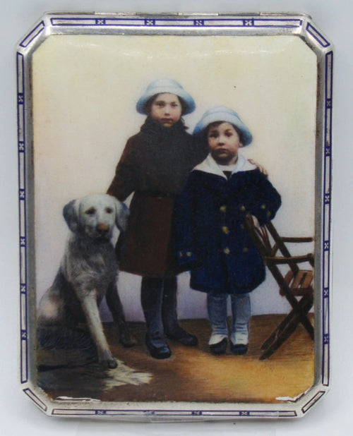 900 silver cigarette case with a colourful scene of two children and a dog, framed by a blue-and-white border.