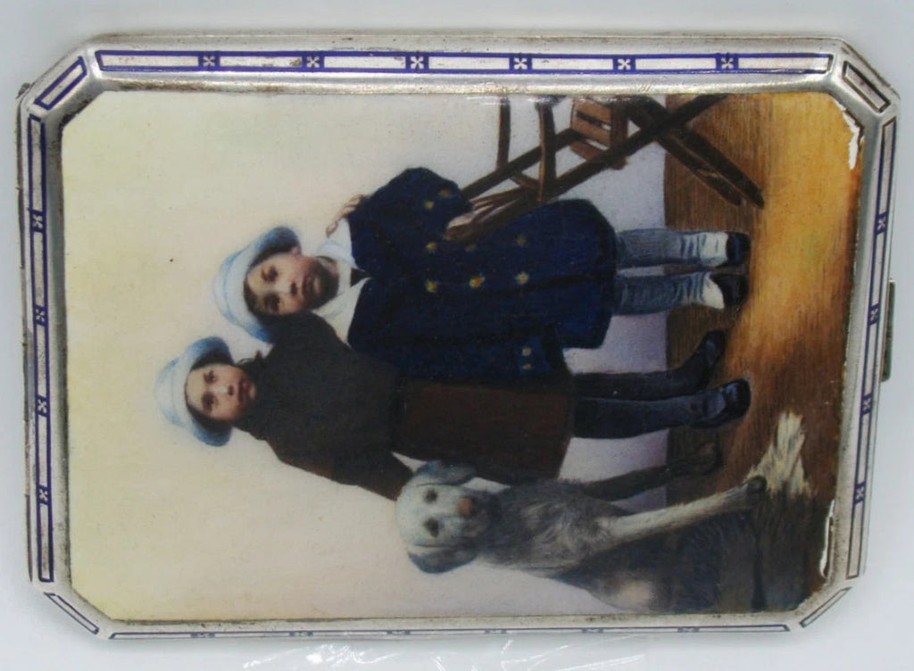 Sideways view of the decorated cigarette case showing two children, a dog and the geometric border.