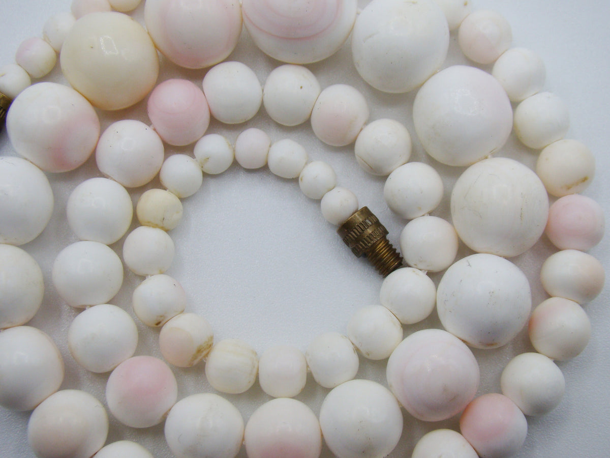 Close-up of pale coral beads and the open gold-tone screw clasp