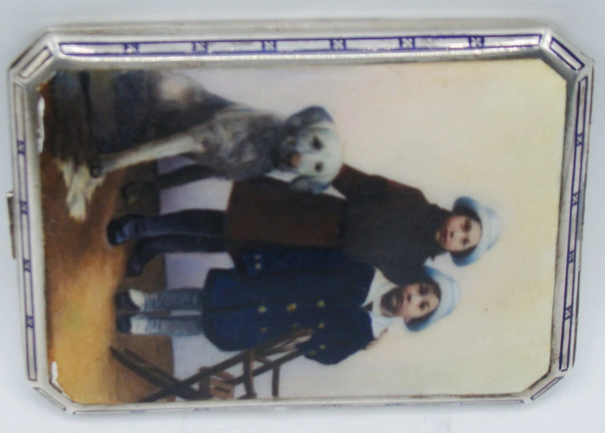 Alternate sideways view of the pictorial silver case showing its blue-and-white border and clipped corners.