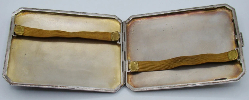 Open silver cigarette case showing the hinged interior and two discoloured retaining straps.