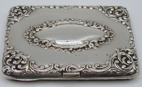 Antique silver cigarette case with raised scrolling decoration and an oval cartouche, viewed from the clasp side.