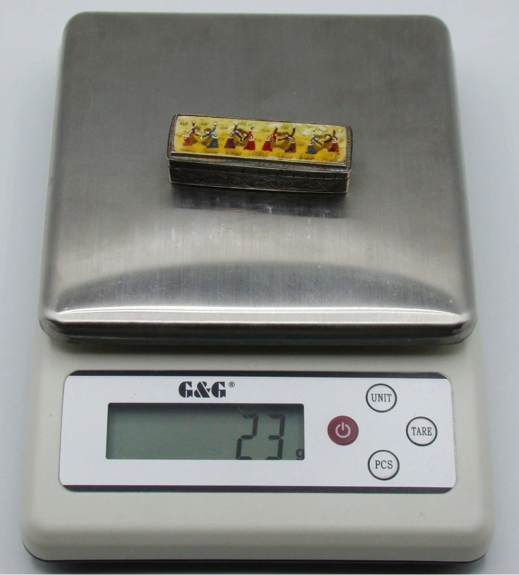 Miniature silver and enamel-on-bone box on a digital scale displaying 23 grams