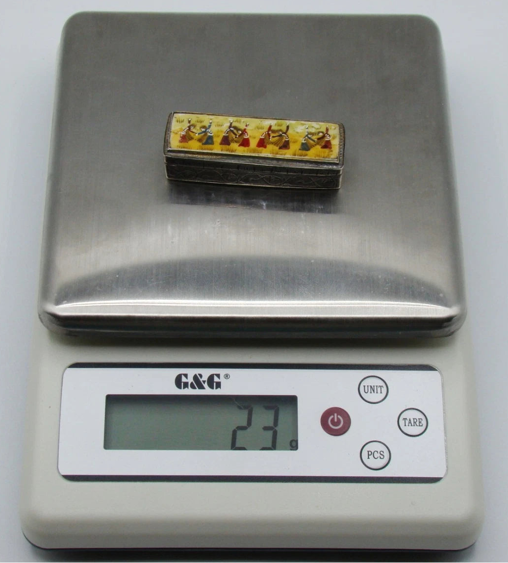 Miniature silver and enamel-on-bone box on a digital scale displaying 23 grams