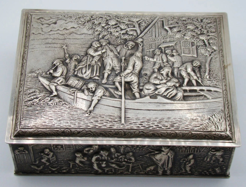 Front view of the silver box with figures aboard a boat on the lid and detailed relief decoration below.