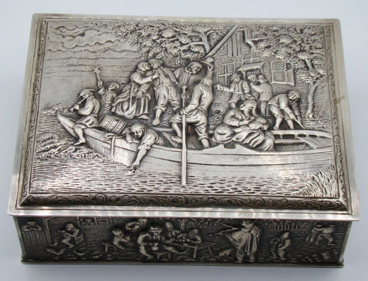 Front view of the silver box with figures aboard a boat on the lid and detailed relief decoration below.