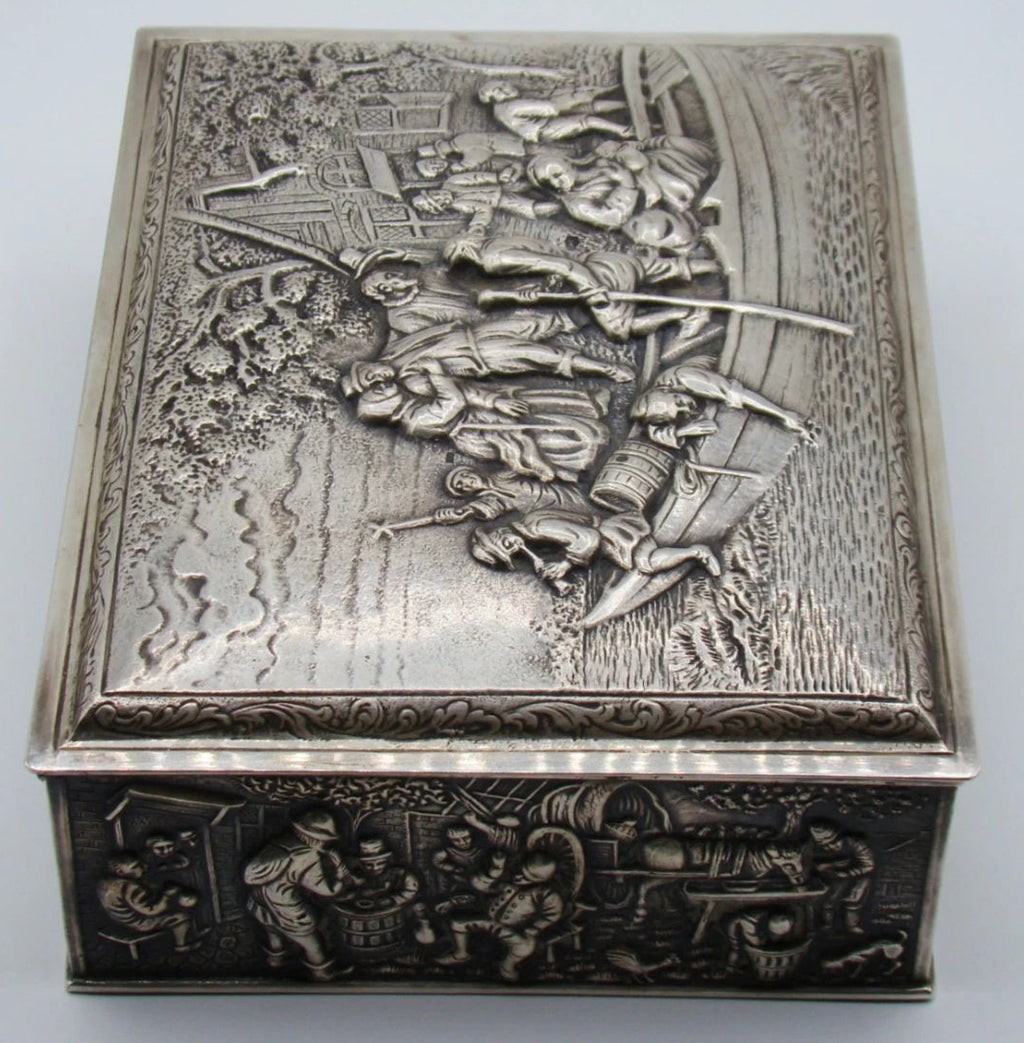 Angled view of the silver box showing the scrolling lid border and figurative side panel.