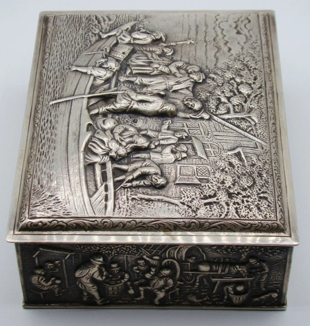 Side view of the silver box showing figures gathered around barrels and a table in relief.