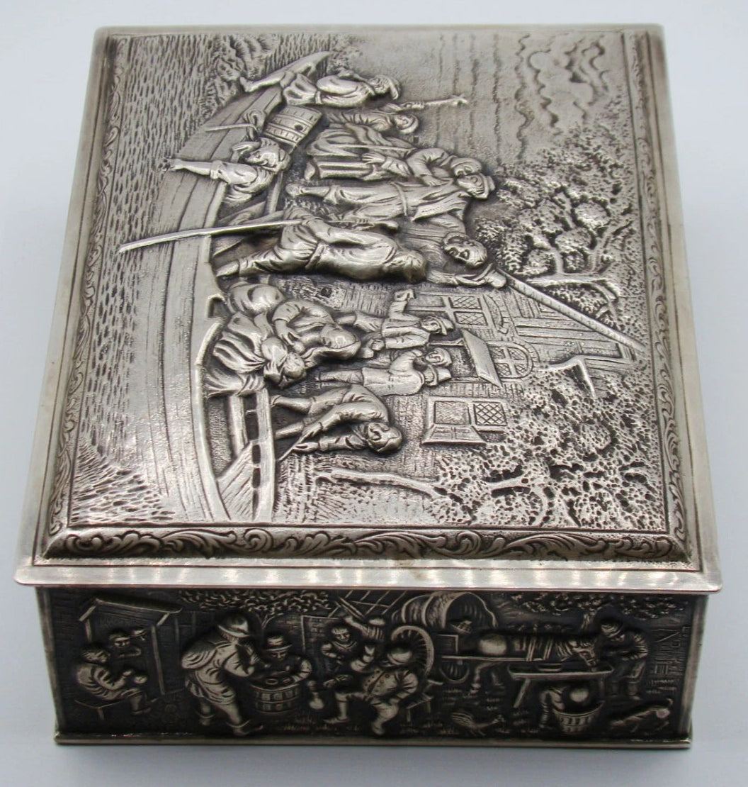 Side view of the silver box showing figures gathered around barrels and a table in relief.
