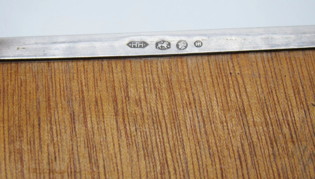 Close-up of four stamped marks on the silver underside rim beside the wooden base panel.
