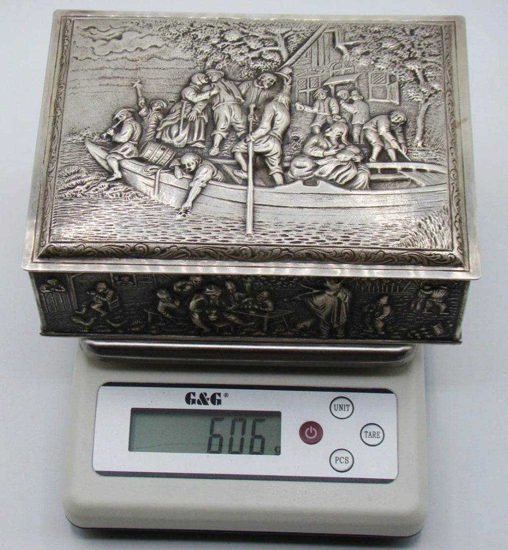 Decorated silver box on a digital scale reading 606 grams, including its wooden components.