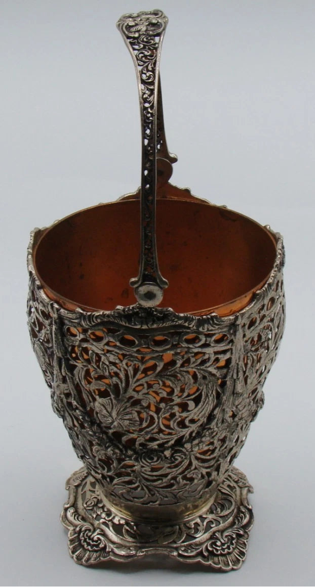 Angled view of the silver basket showing its decorated handle and pierced foliate body with insert.