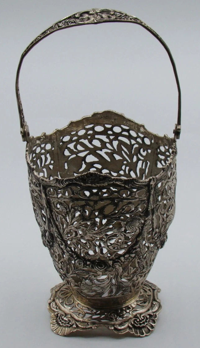 Silver basket without its insert, revealing the pierced foliate openwork and raised swing handle.