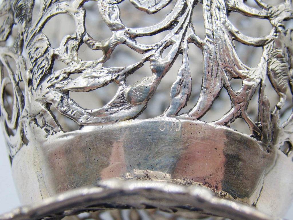 Close-up of the 800 stamp on the silver basket beside its pierced leaf decoration.