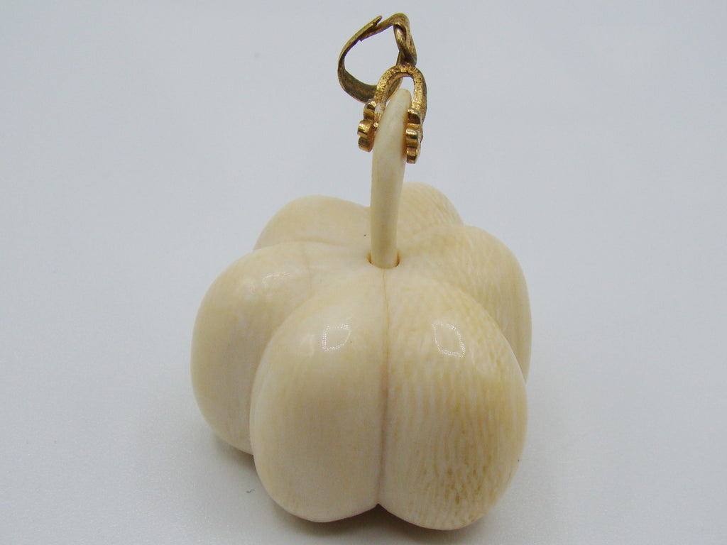 A carved ivory or bone pendant shaped like a small flower or bud with a gold-tone loop at the top, photographed on a plain light background.