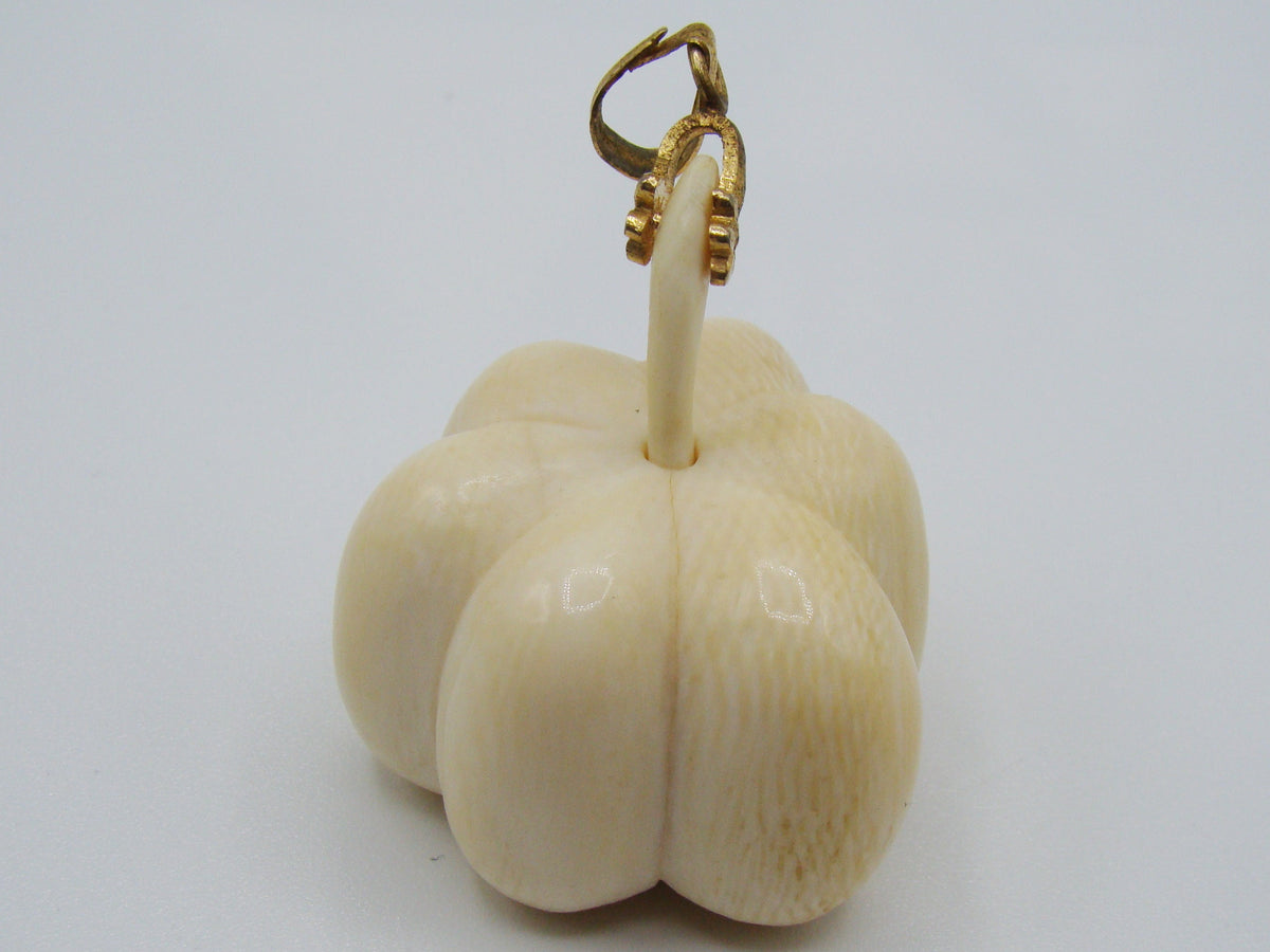 A carved ivory or bone pendant shaped like a small flower or bud with a gold-tone loop at the top, photographed on a plain light background.