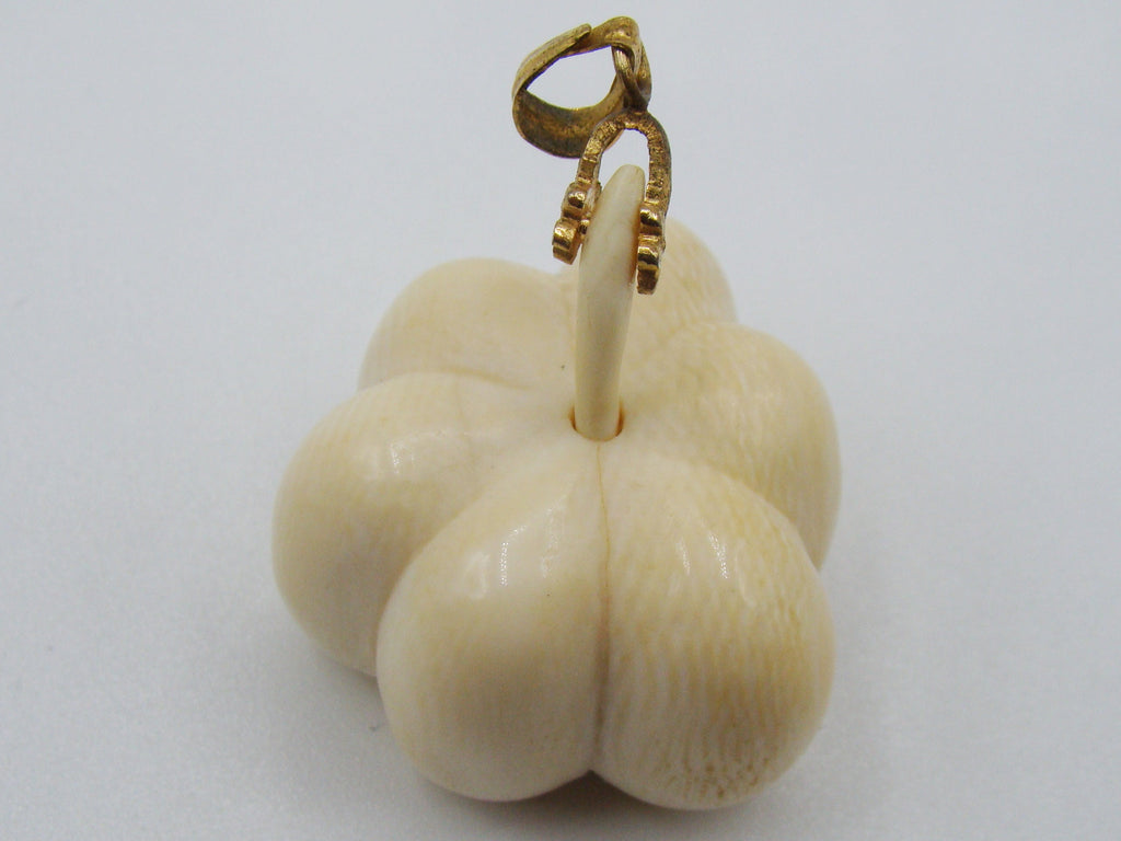 A cream-colored carved ivory figurine shaped like a flower bud with a small gold-colored loop at the top, set against a plain light gray background.