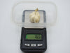 A small cream-colored decorative pumpkin figurine with a gold stem, shown on a digital scale displaying 16.5g, with a clear plastic lid resting on top, set against a plain white background.