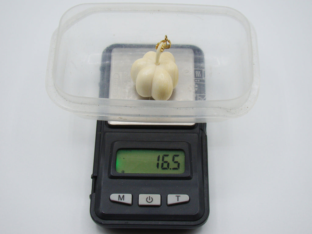 A small cream-colored decorative pumpkin figurine with a gold stem, shown on a digital scale displaying 16.5g, with a clear plastic lid resting on top, set against a plain white background.