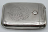 Angled front view of the silver cigarette case showing scrolling foliate engraving and surface wear.