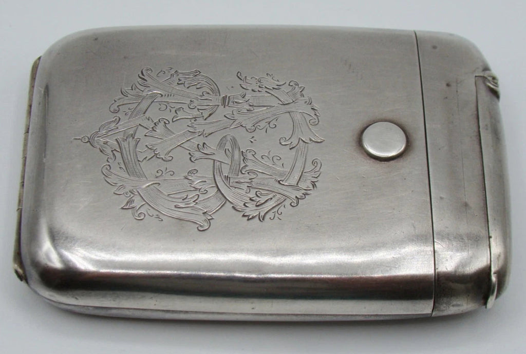 Angled front view of the silver cigarette case showing scrolling foliate engraving and surface wear.