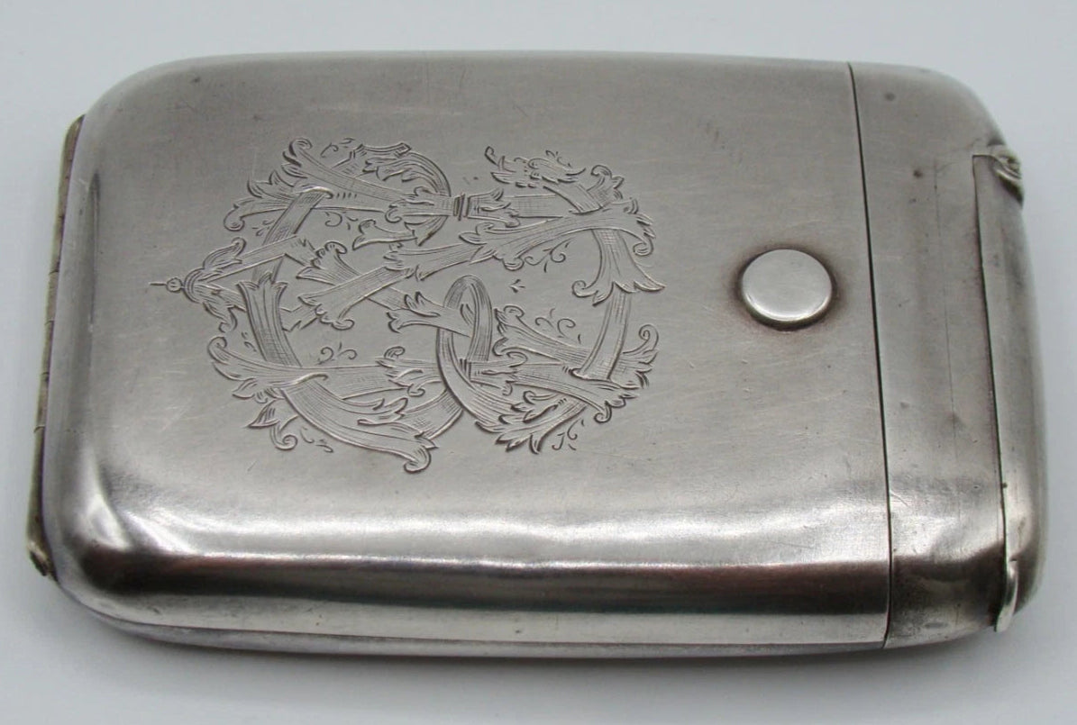 Angled front view of the silver cigarette case showing scrolling foliate engraving and surface wear.