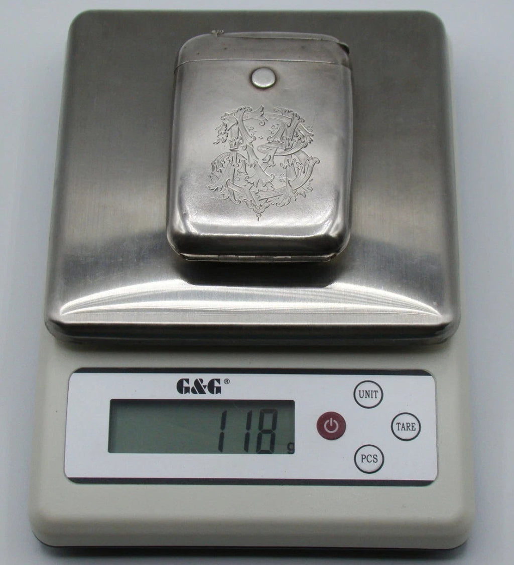 Monogrammed silver cigarette case on a digital scale displaying 118 grams.