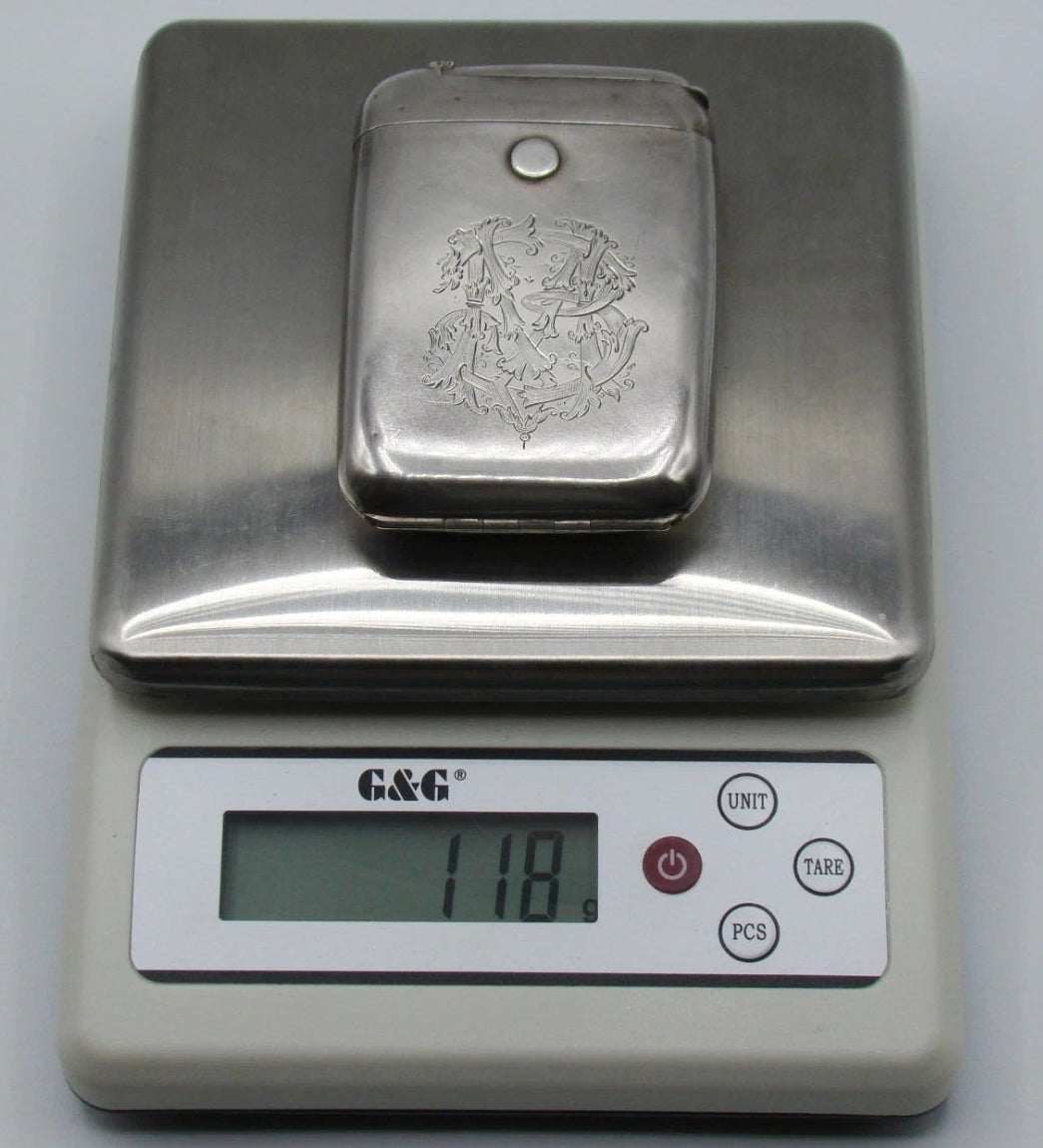 Monogrammed silver cigarette case on a digital scale displaying 118 grams.