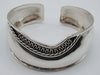 Front of 925 silver open cuff bracelet with looping scroll ornament against a darkened ground.