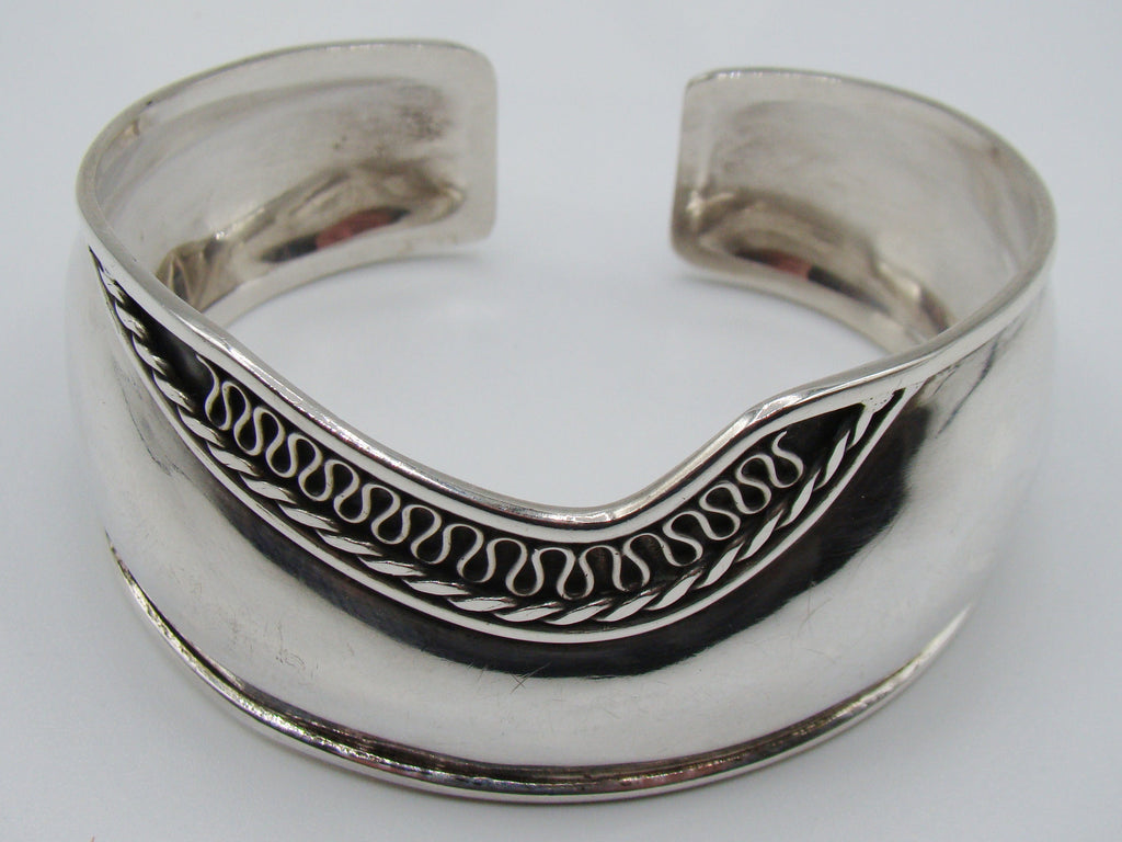 Front of 925 silver open cuff bracelet with looping scroll ornament against a darkened ground.