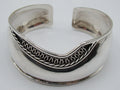 Front of 925 silver open cuff bracelet with looping scroll ornament against a darkened ground.