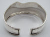 Angled view of the silver cuff bracelet showing the scroll band and smooth reflective lower section.