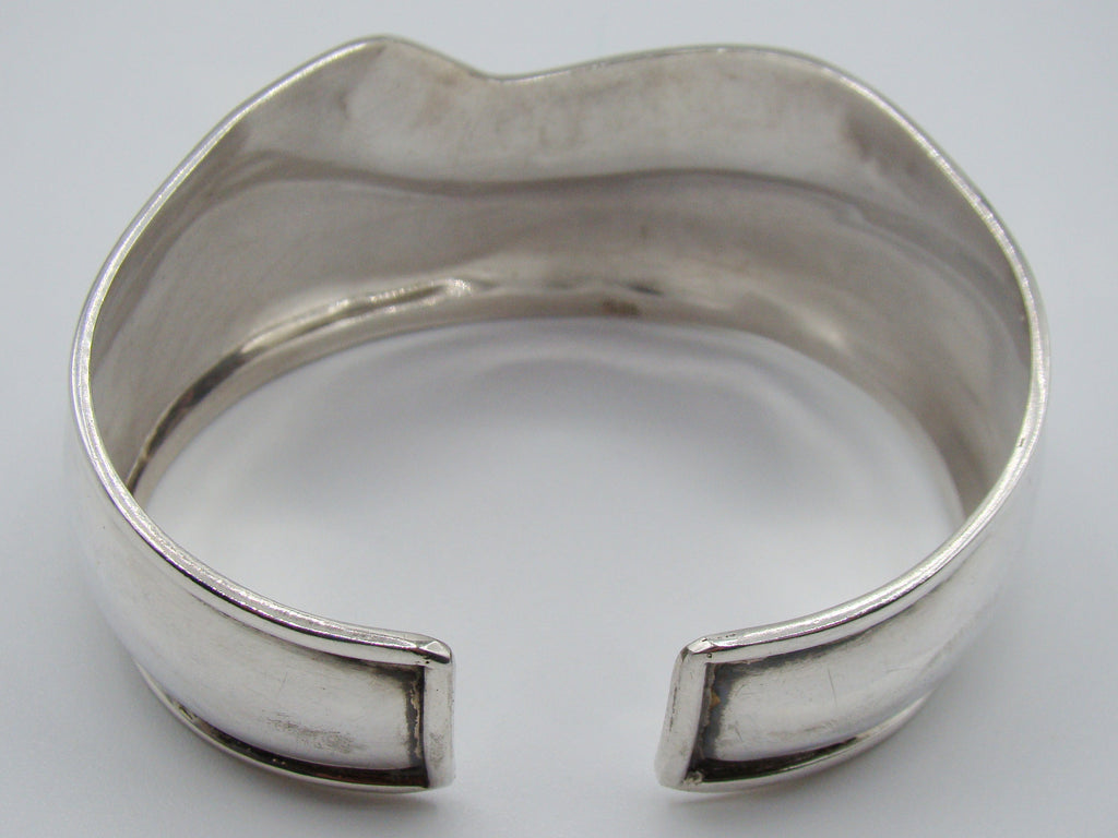 Angled view of the silver cuff bracelet showing the scroll band and smooth reflective lower section.