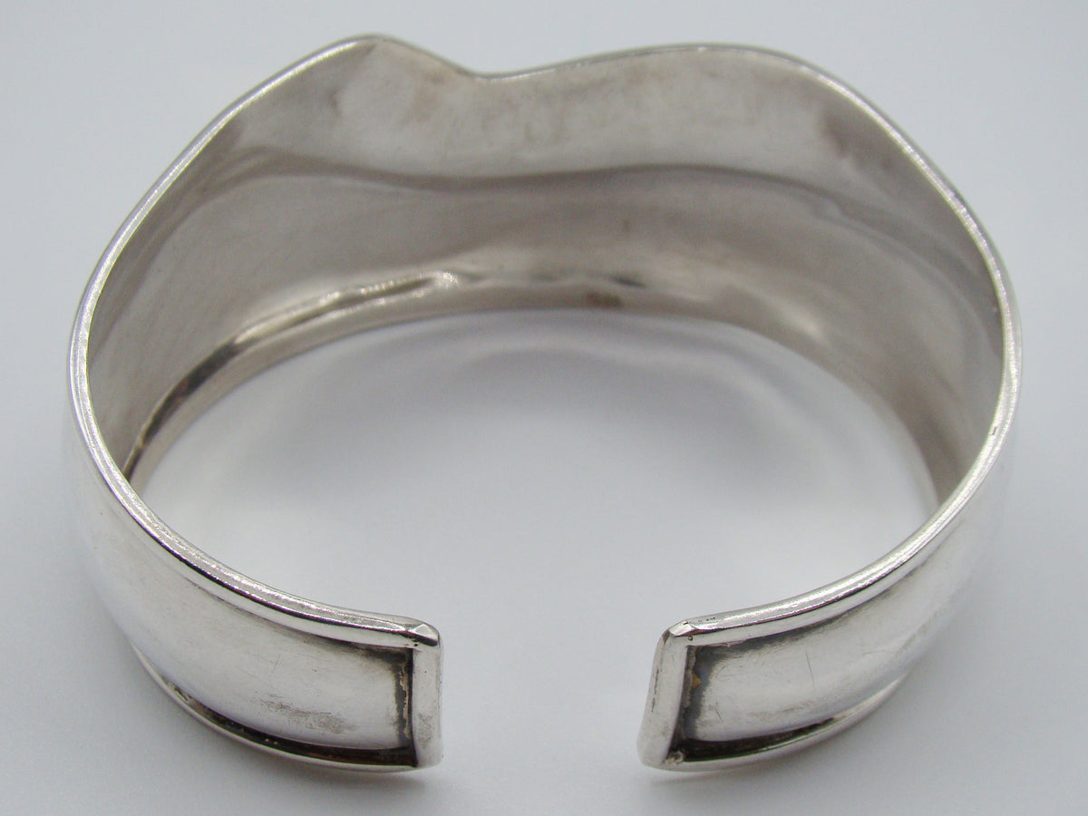 Angled view of the silver cuff bracelet showing the scroll band and smooth reflective lower section.