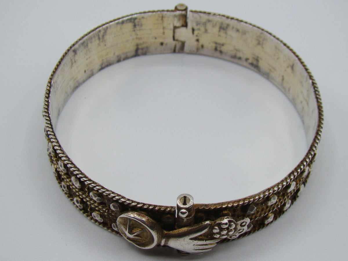 Silver hinged bangle with sculpted hand-motif fastening, round bird detail, and rope-like borders.