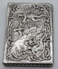 Vertical view of the silver box showing the raised figures and ornate scrolling lid border.