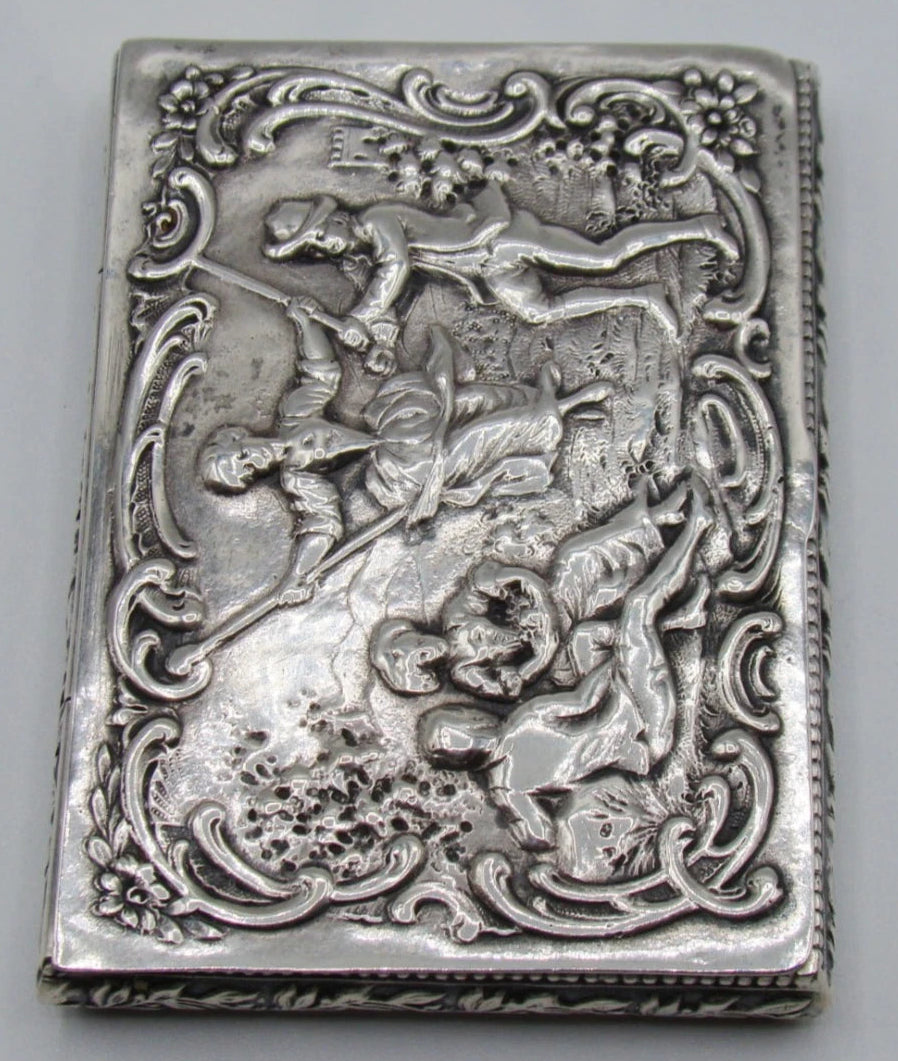 Vertical view of the silver box showing the raised figures and ornate scrolling lid border.