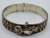 Angled front view of the silver bangle showing the hand fastening and rows of raised metal accents.