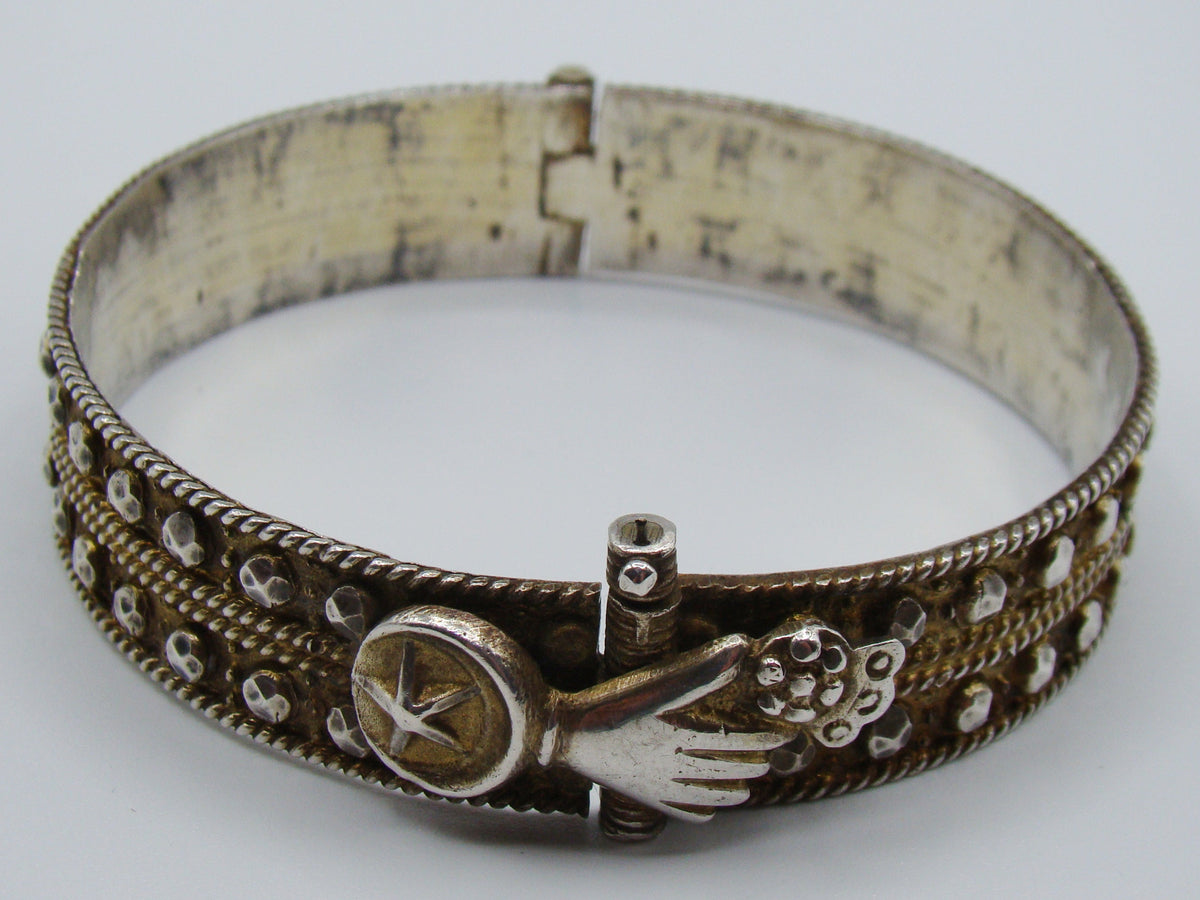 Angled front view of the silver bangle showing the hand fastening and rows of raised metal accents.