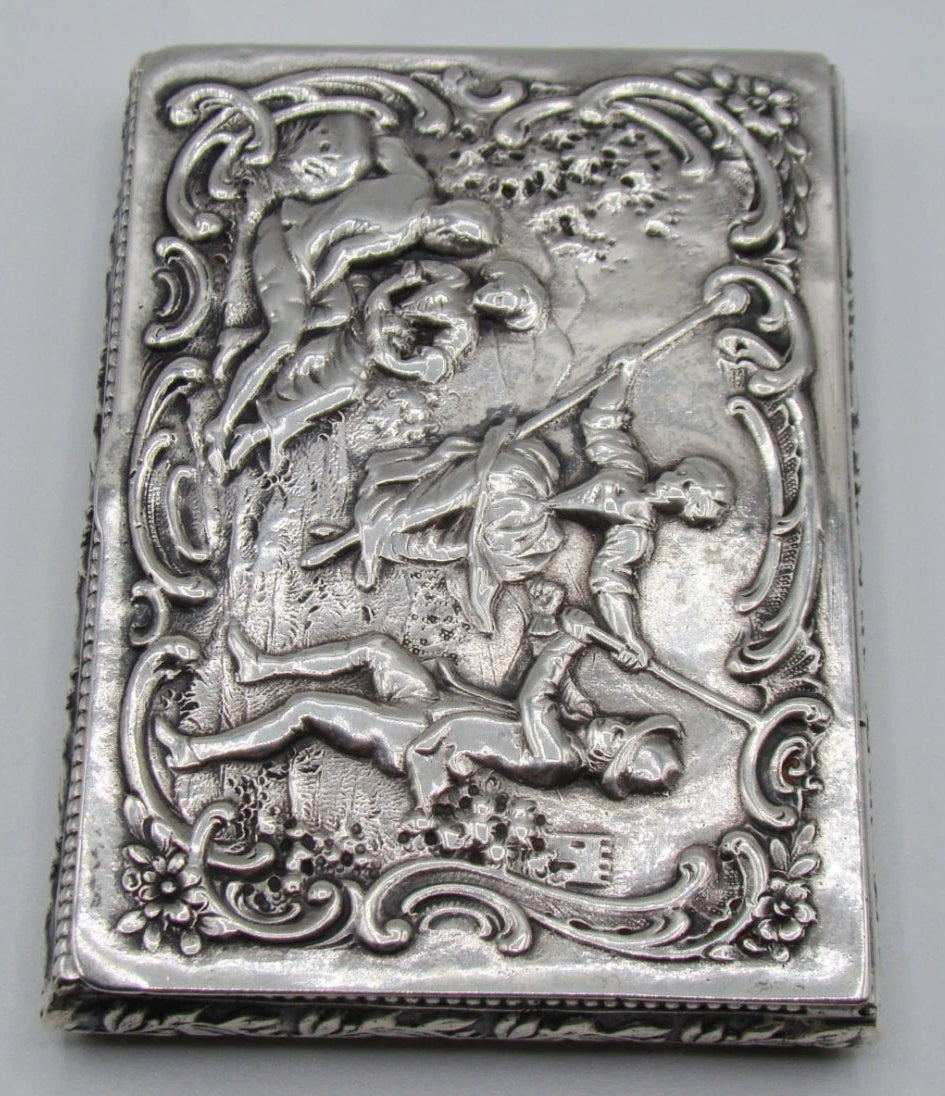 Close view of the silver box showing the figurative relief, flowers, and beaded edge.