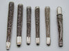 Six antique silver filigree mouthpieces arranged side by side, showing scrolling wire decoration and smooth ends