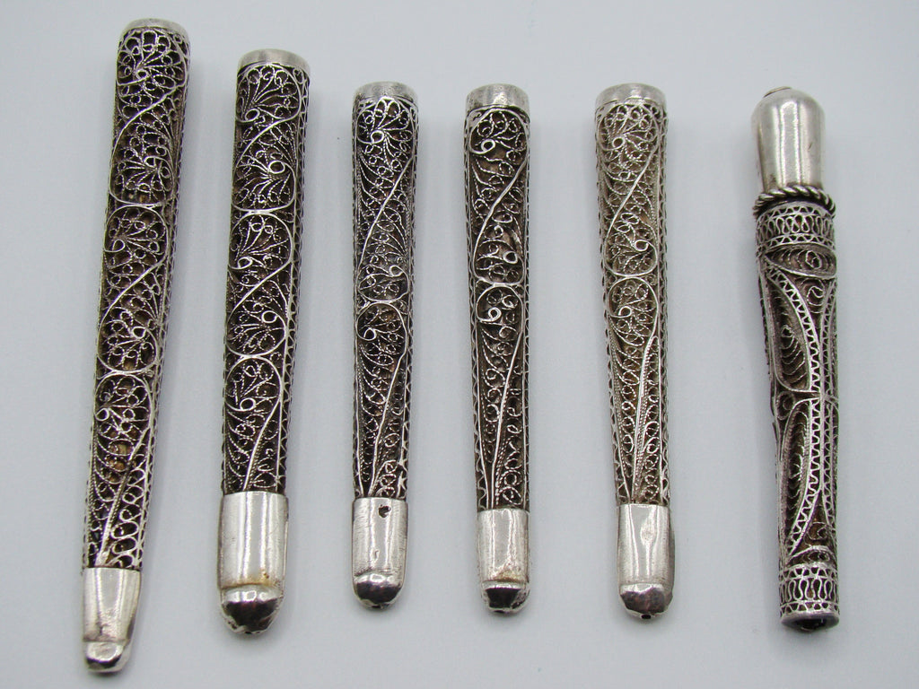 Six antique silver filigree mouthpieces arranged side by side, showing scrolling wire decoration and smooth ends